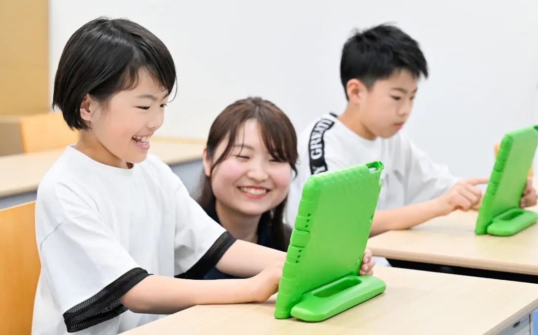 笑顔でプログラミングを学ぶ子どもと講師